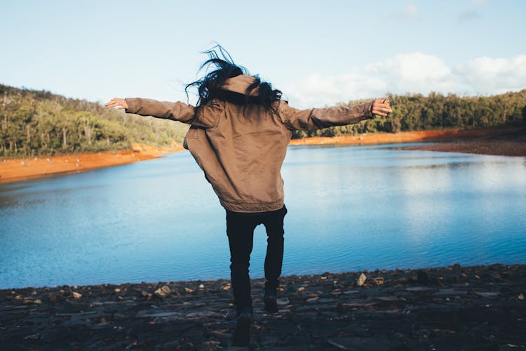 Faceless Person In Outerwear Jumping Happily On Lake Shore