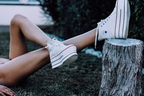 Unrecognizable woman tying in forest with legs on tree stub