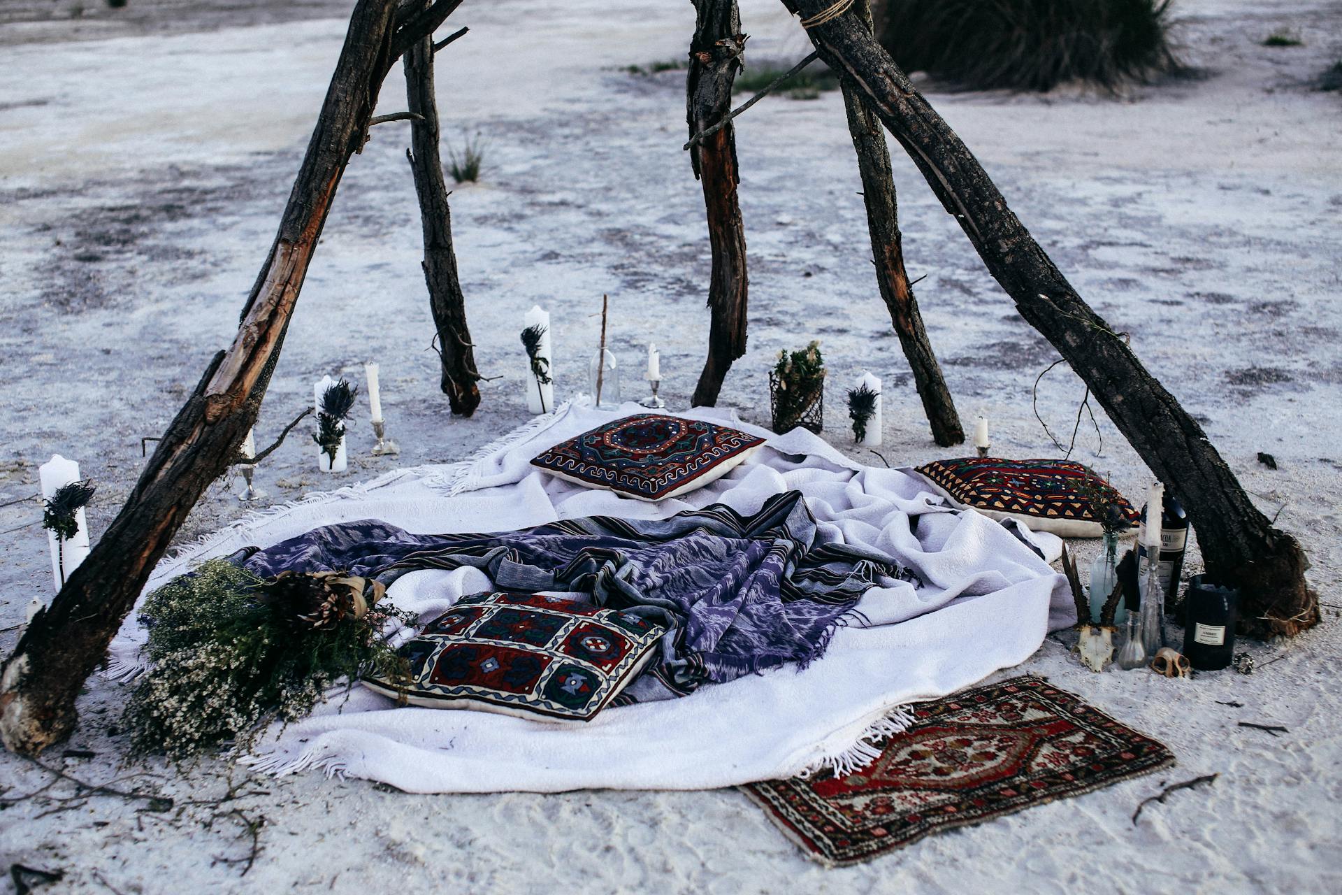 Rustic outdoor picnic setup with blankets, pillows, and candlesticks under a canopy.