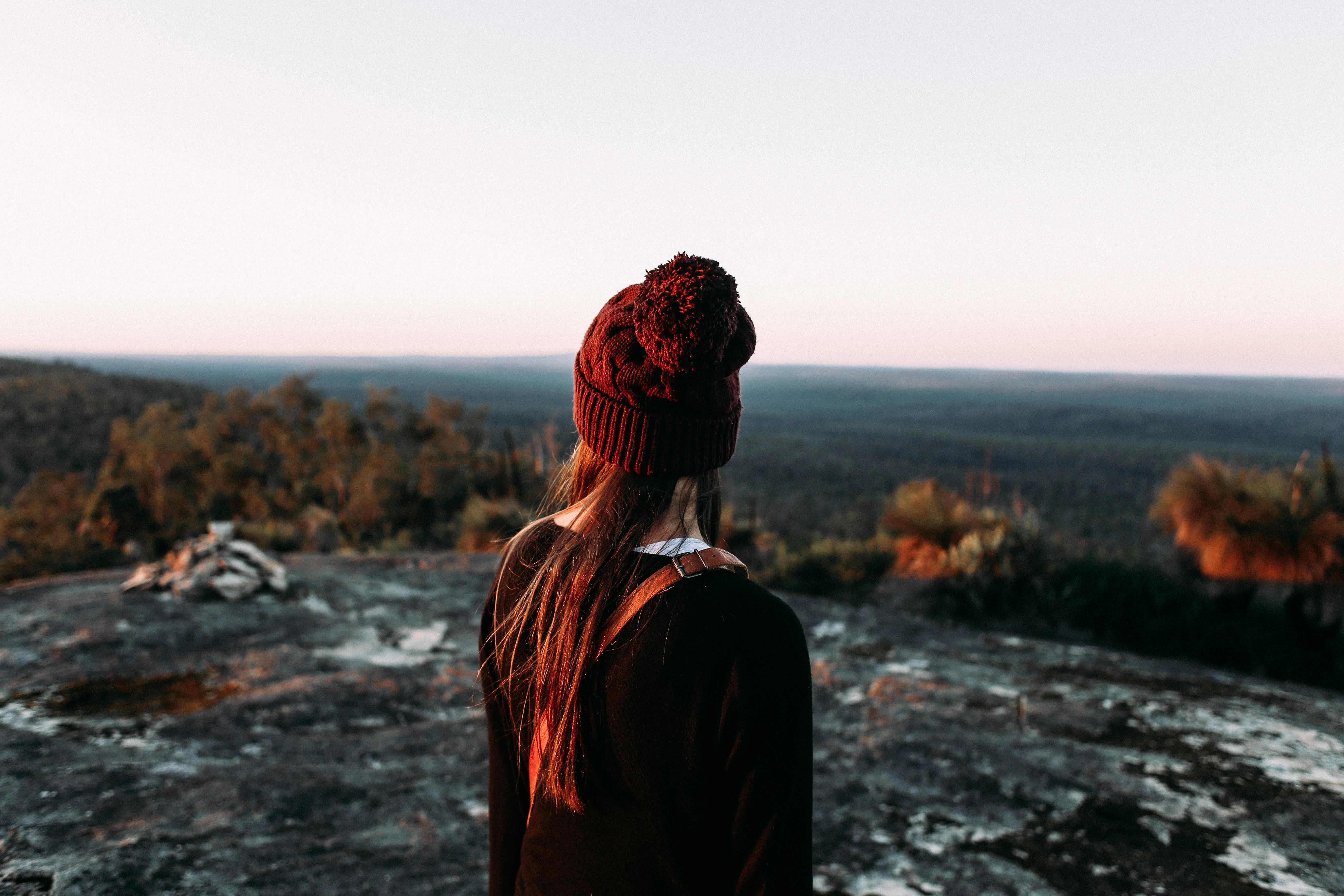 一位身着冬装的女人站在岩石地上，欣赏着日落时分广阔的森林地平线