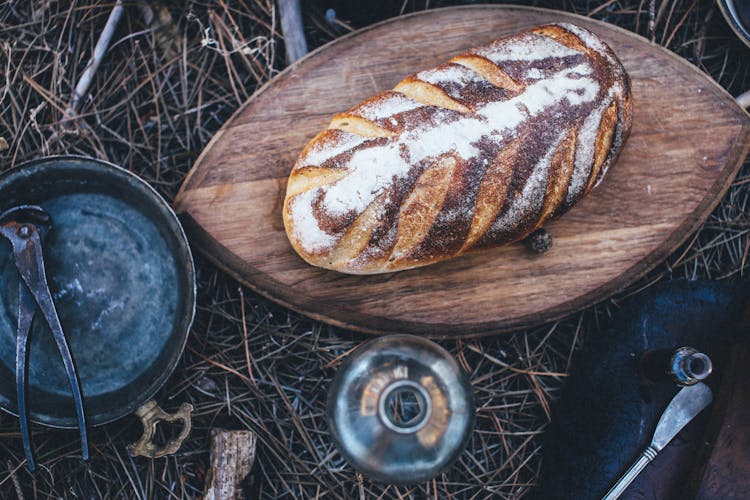 Bread On Cutting Board And Pan With Pliers On Grass