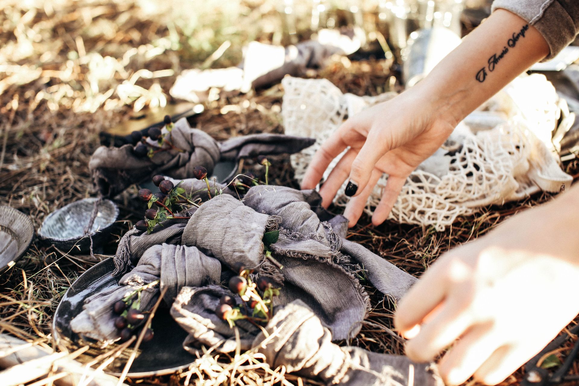 Crop faceless female setting decorative napkins with herbs on dry grassy meadow near utensil and reusable bag while having picnic in sunny day in nature