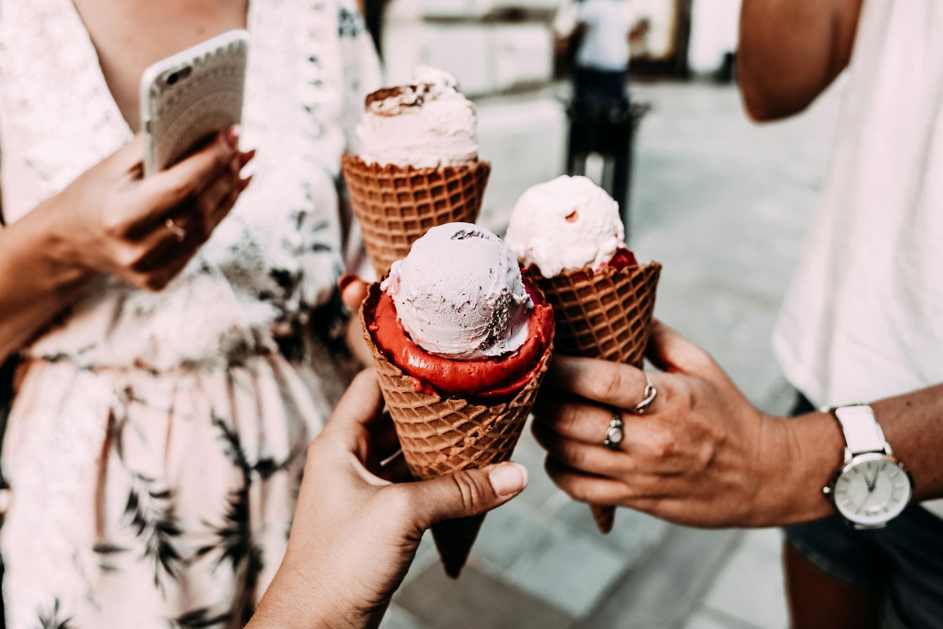 Crop anonymous friends in casual summer clothes clinking delicious cone ice creams while gathering on street