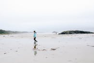 Unrecognizable person in outerwear walking on wet misty seashore