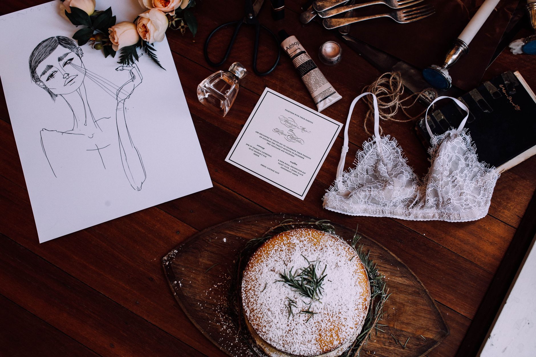 Overhead flat-lay of a rustic semi-naked wedding cake with dried pampas grass, fresh figs, blackberries, and eucalyptus sprigs arranged around the base on a raw linen table runner