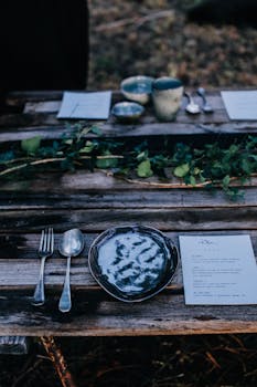 A rustic outdoor dining table with a plate, silverware, and a menu in a natural woodland setting.