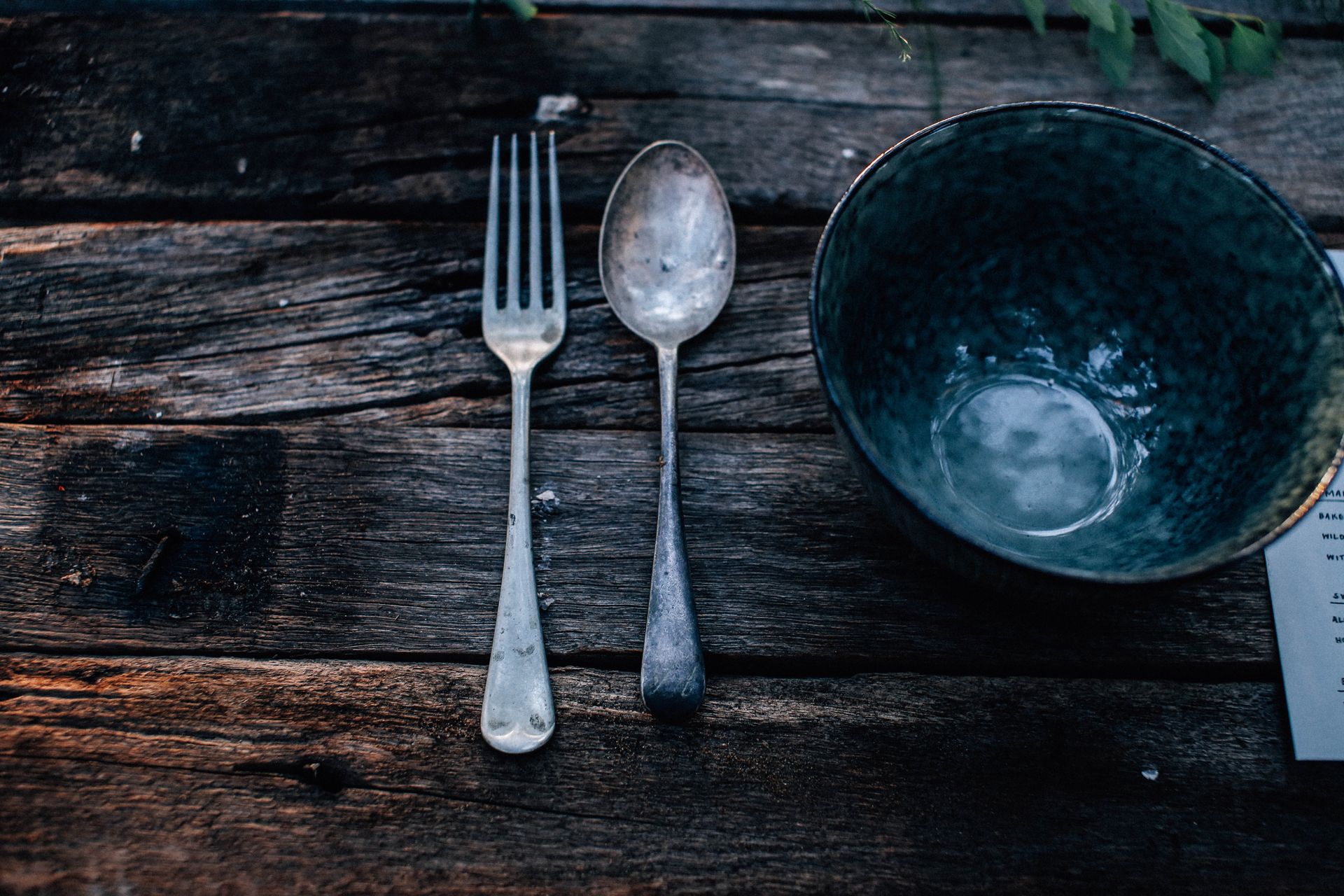 High angle of round shaped bowl near fork and spoon on rough wooden table in daytime