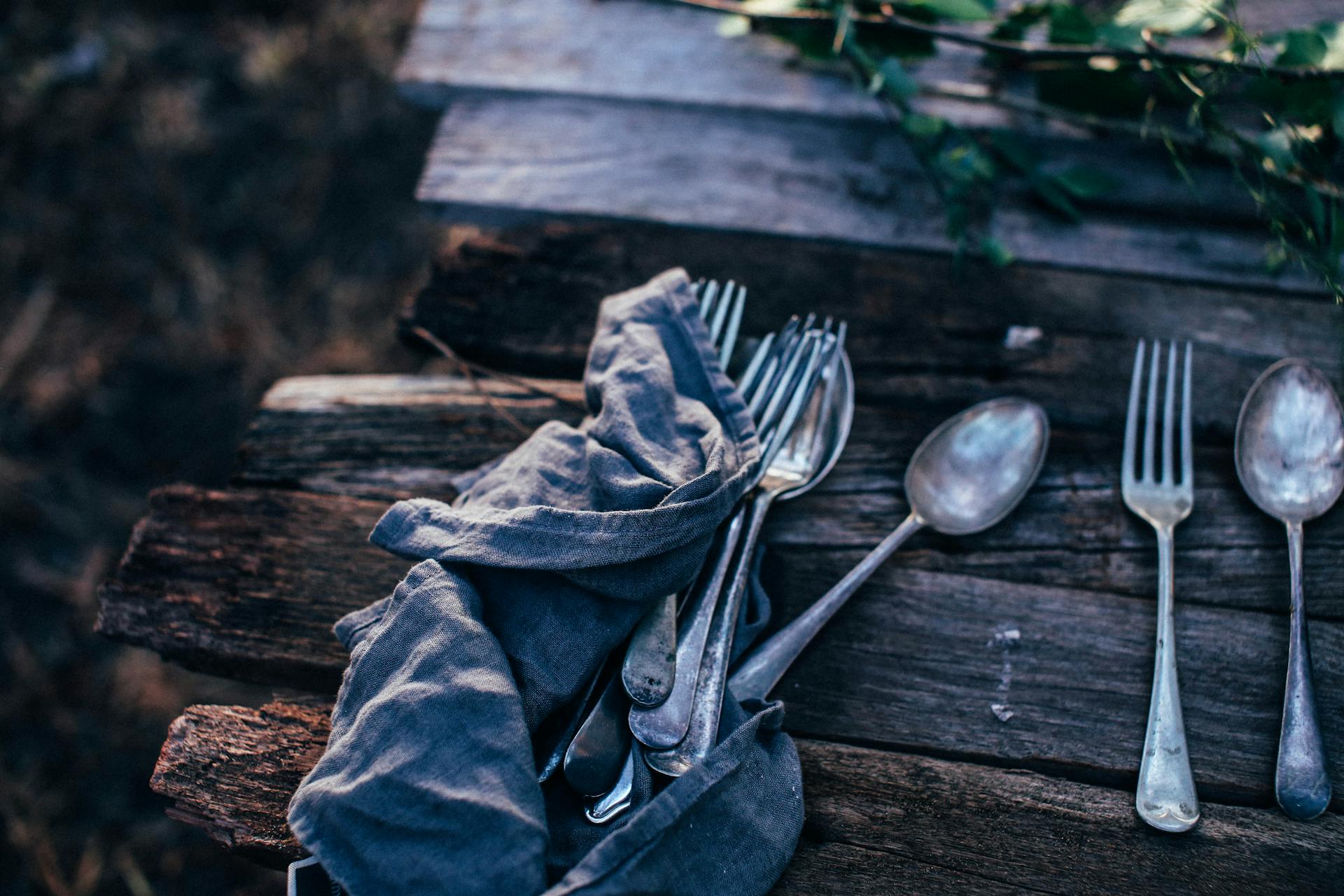High angle of spoons with forks near crumpled textile on rustic table in garden on sunny day