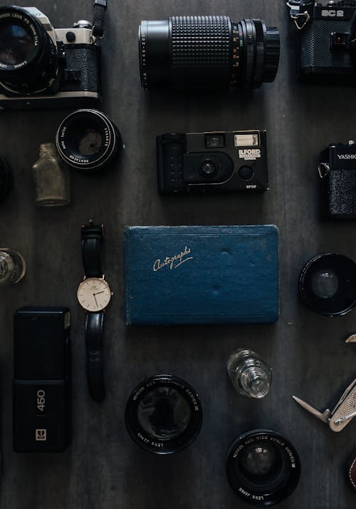 Free Top view of notebook among wristwatch and assorted retro photo cameras with accessories on gray background Stock Photo