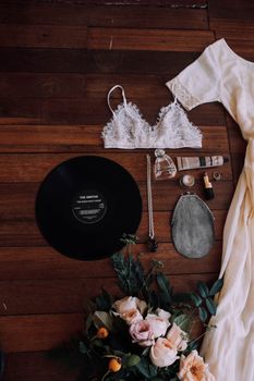 Top view of white retro dress near lace brassiere and beauty products with blooming flowers on wooden floor