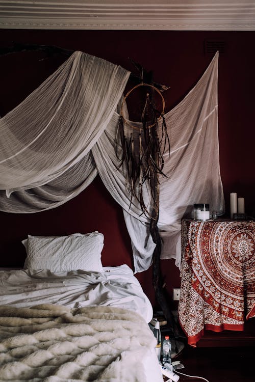 Free Unmade bed with soft pillow and pleated plaid under fabrics and dream catcher in house Stock Photo