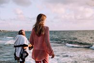 Anonymous siblings contemplating wavy sea under cloudy sky