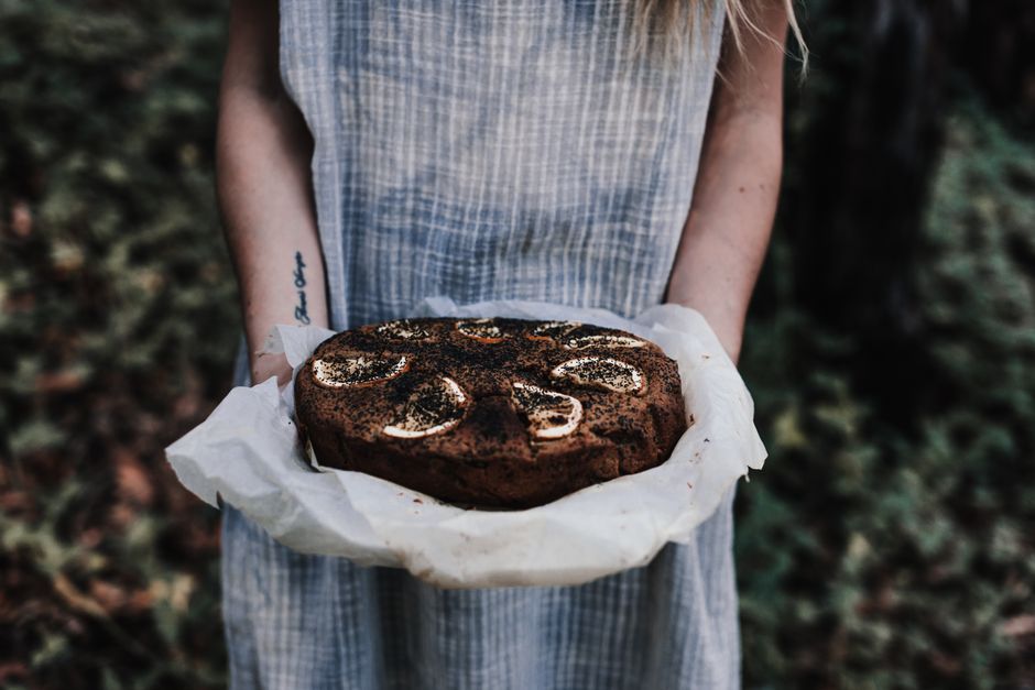 Crop unrecognizable female with tattoo and tasty chocolate cake with lemon slices on top outdoors