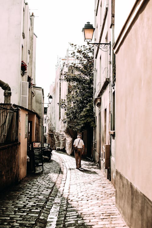 Unrecognizable man walking on narrow street between urban buildings
