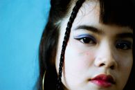 特写镜头中，一位年轻女子留着辫子，妆容鲜艳，背景为蓝色