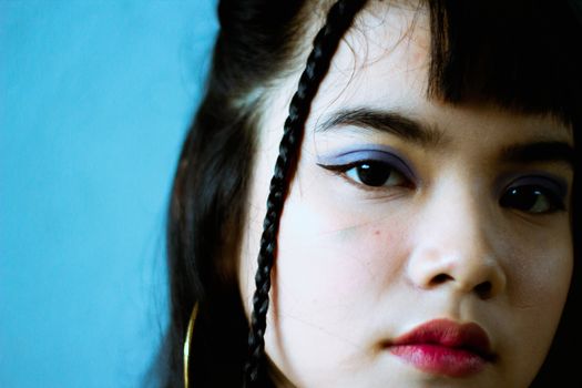 特写镜头中，一位年轻女子留着辫子，妆容鲜艳，背景为蓝色