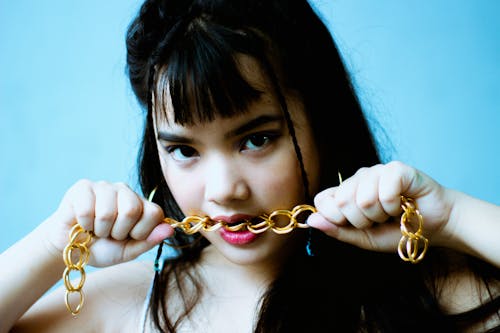A Female Teenager Holding Gold Chain in Her Mouth


