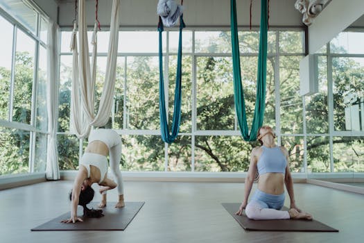 Women exercising on yoga mats in a studio with aerial silks, focus on flexibility and wellness.
