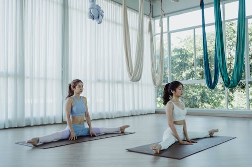 Free Two Women Practising Split Legs on a Yoga Mat Stock Photo