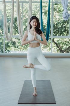 An Asian woman in sportswear practicing yoga indoors in a serene studio environment for a healthy lifestyle.