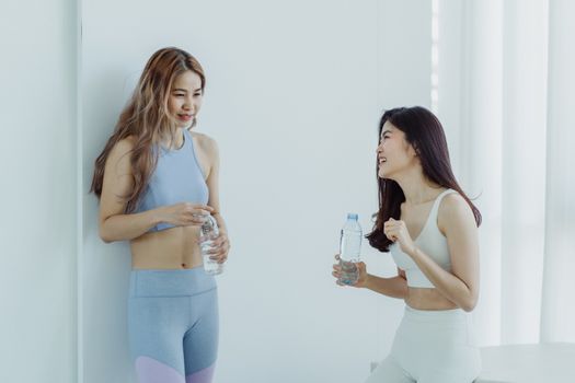 两名穿着运动服的亚洲女性在健身休息时拿着水瓶聊天