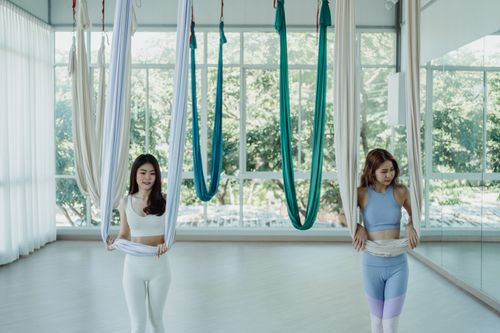 Free Two women using aerial silks for yoga in a bright studio. Embracing fitness and healthy lifestyle. Stock Photo