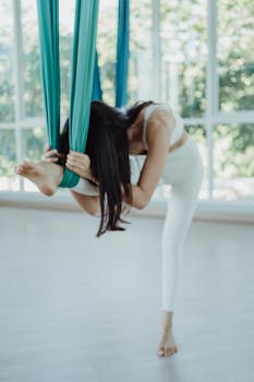 Asian woman practicing aerial yoga in bright studio, embracing a healthy lifestyle.