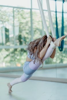 Asian woman performing aerial yoga in a sunlit studio, showcasing fitness and flexibility.