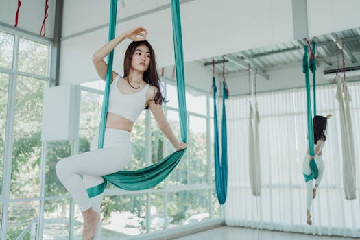 Asian woman practicing aerial yoga in a bright studio, embodying elegance and fitness.