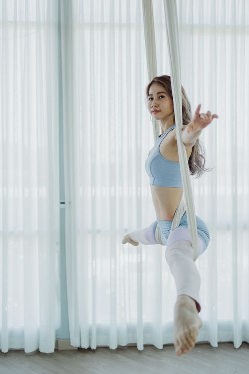 Free Woman performing an elegant aerial yoga pose in a sunlit studio, showcasing strength and balance. Stock Photo