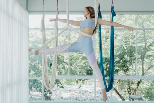 Woman practicing aerial yoga in a bright, serene studio with natural views.