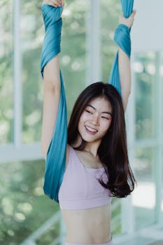Smiling Asian woman enjoying aerial yoga workout, showcasing fitness and healthy lifestyle.