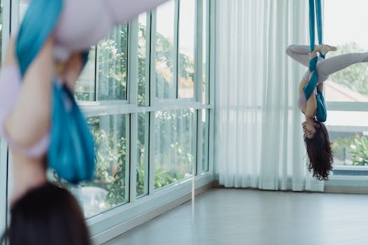 Woman performing aerial yoga, showcasing a graceful pose in a bright studio with natural light.