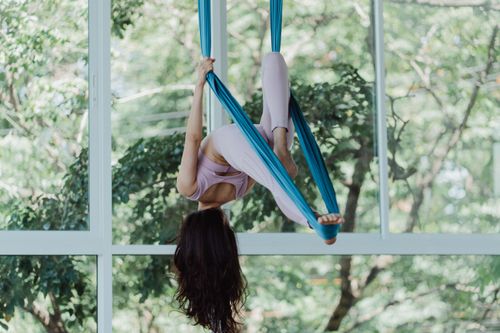 Free Woman practicing aerial yoga using silk hammock by large window indoors. Stock Photo