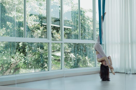 Woman practicing aerial yoga inverted pose in a bright studio with natural light.