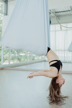 Woman practicing aerial yoga pose in a bright and modern studio for fitness and relaxation.