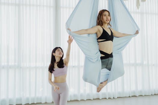 Two women practicing aerial yoga in a bright studio, showcasing strength and flexibility.