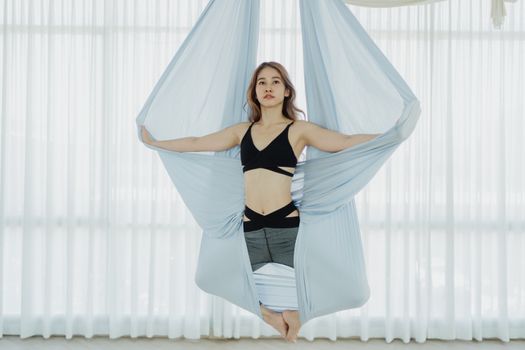 Woman performing aerial yoga in a suspended hammock indoors, showcasing strength and balance.