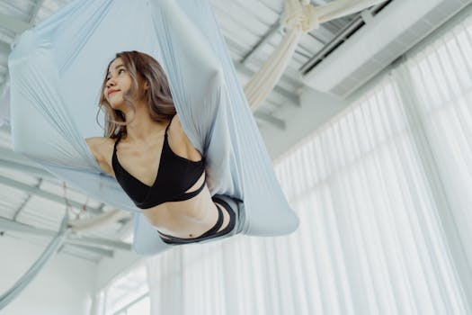 A woman performing an advanced aerial yoga pose in a bright indoor studio, showcasing fitness and elegance.