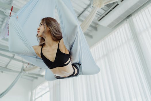 A woman gracefully practices aerial yoga in a bright studio, showcasing fitness and flexibility.