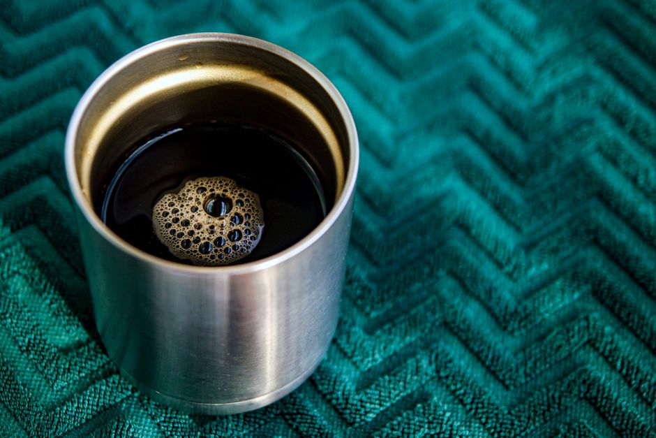 A stainless steel cup filled with black coffee, set on a textured green surface, highlighting a cozy morning vibe.