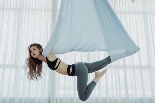 A woman practicing aerial yoga indoors on a hammock, showcasing balance and flexibility.