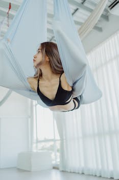 A woman performs aerial yoga in a sunlit studio, showcasing strength and flexibility.