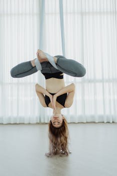 Woman practicing aerial yoga pose indoor, promoting fitness and relaxation.