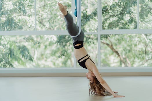 Woman performing an upside-down aerial yoga pose in a sunny studio, displaying flexibility and strength.
