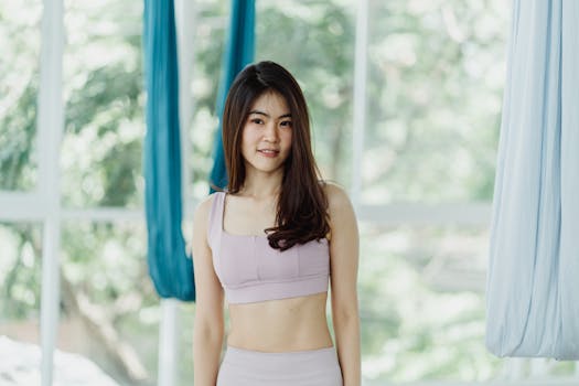 A young woman practicing aerial yoga with silks in a bright, indoor studio. Promotes health and wellness.