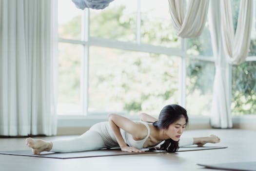 Asian woman performing yoga stretch in a bright, serene indoor setting.