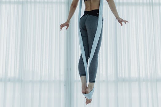 Woman practicing aerial yoga in a bright studio using a sash for flexibility and balance.