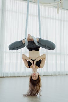 Woman practicing aerial yoga in an upside-down pose, emphasizing balance and flexibility.