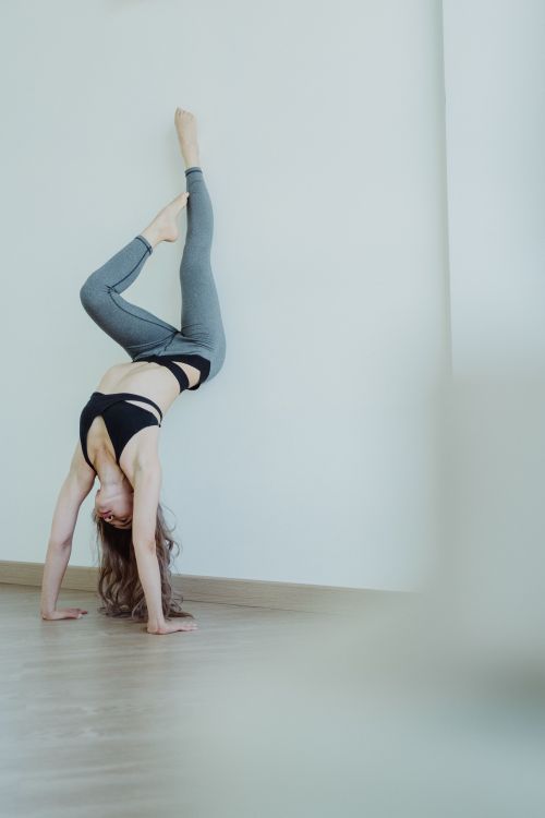 Free A woman in a sports bra and leggings performs a handstand indoors, showcasing flexibility. Stock Photo